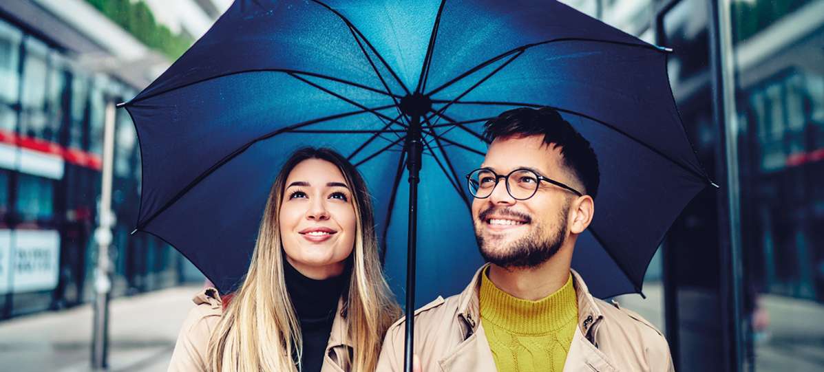 Allianz Partners: Berufsunfähigkeit für Arbeitnehmer:innen: Ein Paar steht unter einem großen blauen Regenschirm.