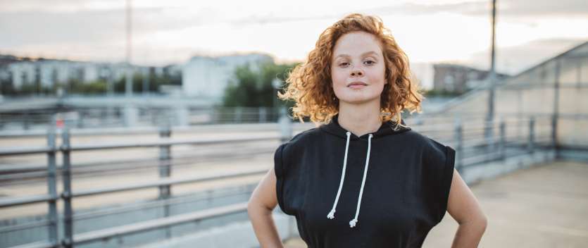 Allianz Pension Partners: Equal Pension. Eine Frau steht mit Händen an den Hüften vor einer Straße und blickt selbstbewusst in die Kamera.