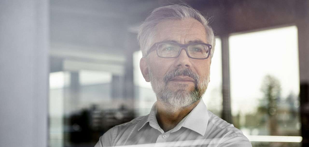 Allianz Pension Partners: Gut vorbereitet in Rente gehen. Ein älterer Herr steht am Fenster und blickt in die Ferne.