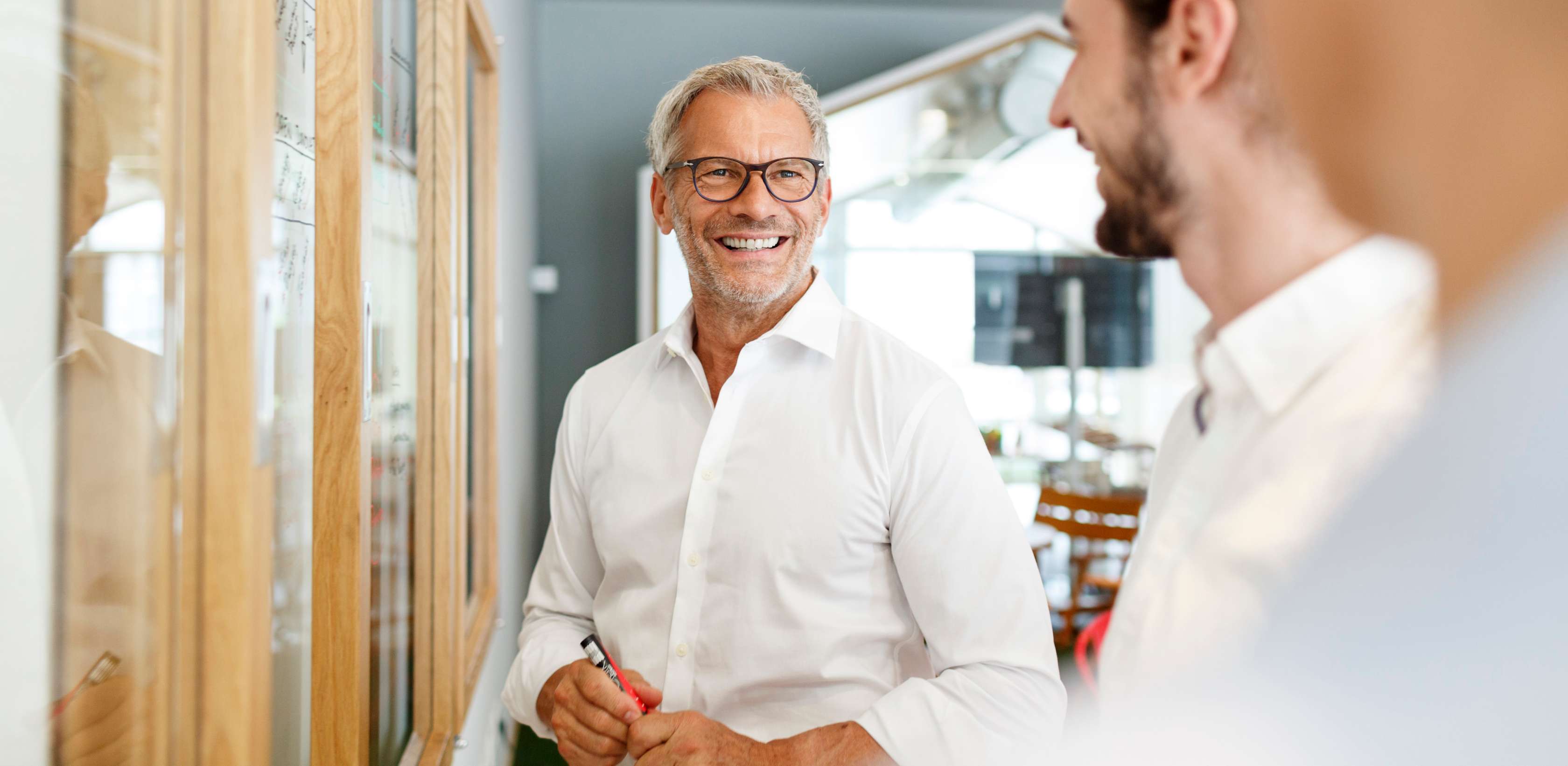 Allianz Pension Partners: Aktueller Benefits-Report. Ein Mann steht im Büro und unterhält sich mit einem Kollegen.